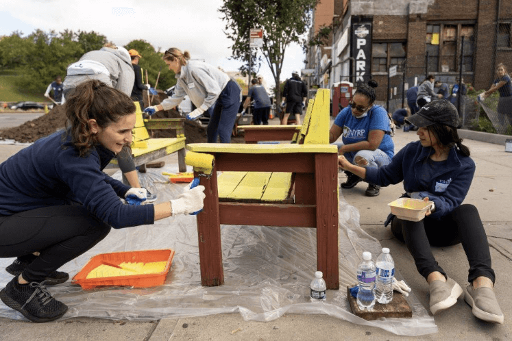 Screen-Shot-2022-04-19-at-4.38.50-PM Three colleagues paint a park bench with yellow paint.